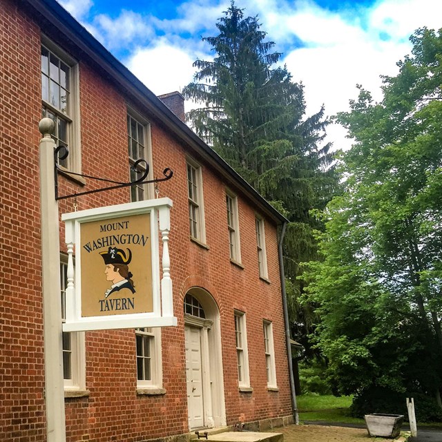 A two story brick tavern with a tavern sign in front