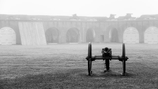 A cannon sits in a foggy parade ground of a fort. 