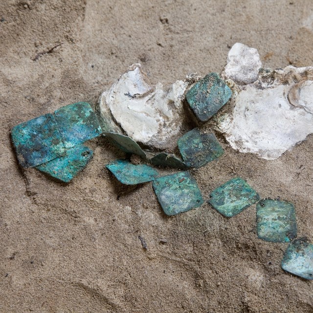 A collection of blue-green copper pendants in sand with seashells nearby