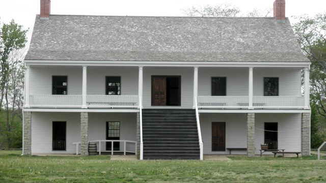 two story building with pillars and chimney on each side with stairway in the middle