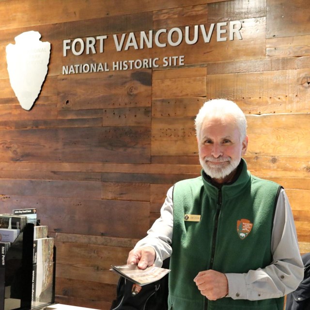 A volunteer dressed in grey and green handing out a Fort Vancouver brochure.