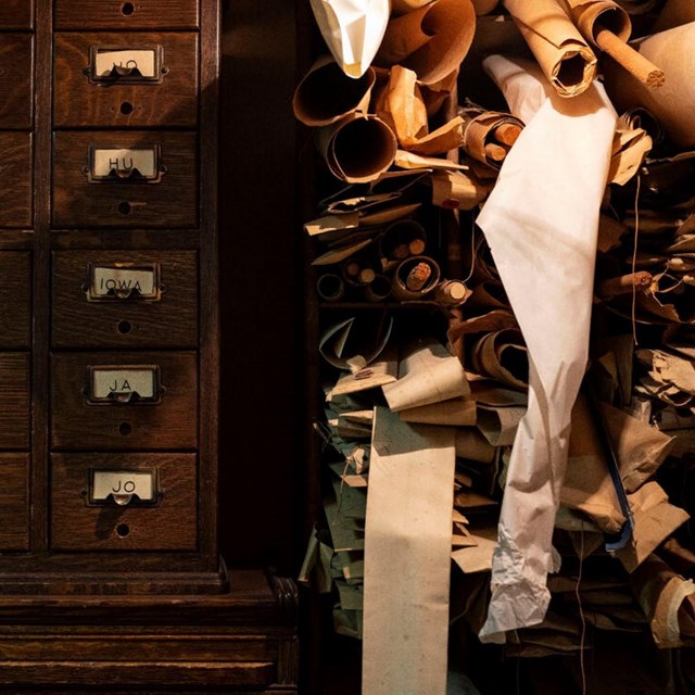 Papers rolled and stacked on top of each other, next to wooden drawers. 