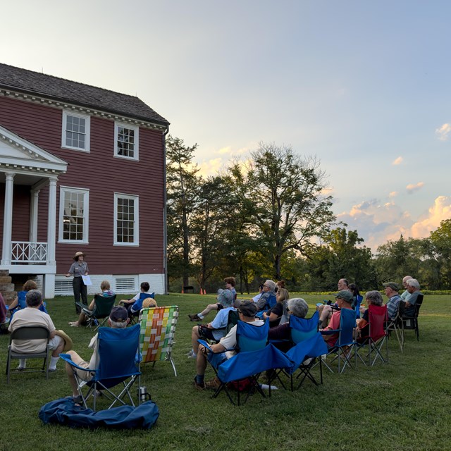 A ranger speaks to people on a lawn outside a historic house.