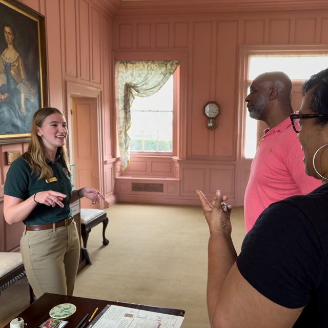 A park volunteer speaking with two people at a visitor center desk.