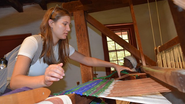 A woman works on a weaving machine. 