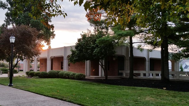 a small, square, brick and concrete, brutalist style building surrounded by trees and grass.  