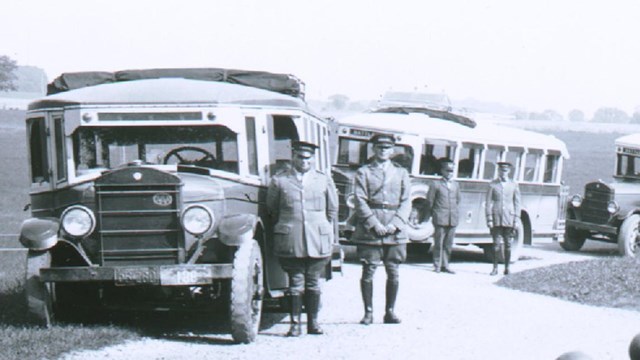 Black and white photograph of four buses, drivers, and Licensed Battlefield Guide circa late 1920s.