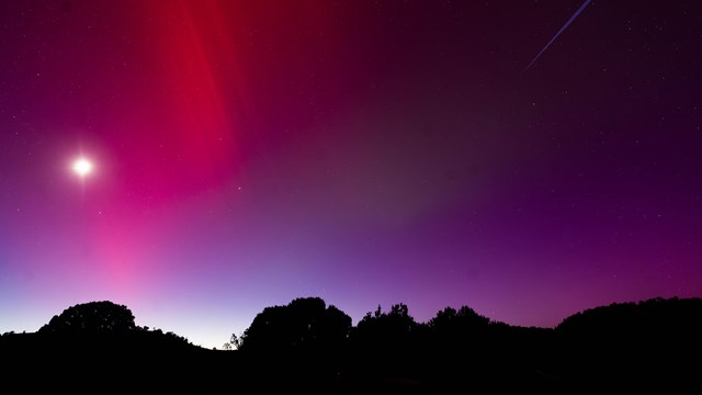 A night sky is illuminated by a vibrant aurora borealis displaying deep red and purple hues.