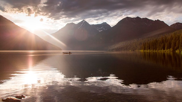  A sunrise over a lake surrounded by mountains with a lone boater on the lake.