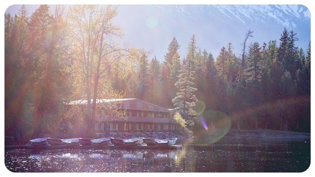 A large hotel sits next to a lake with mountains behind. 