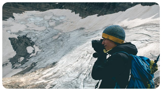 A person stands in front of a mountain glacier. 