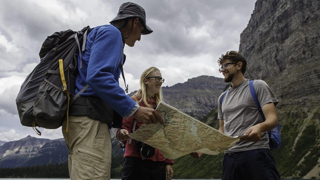 Three visitors looking at a map in front of mountains.