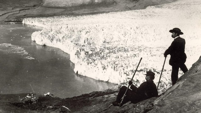 Two people look down at a huge tidewater glacier from a mountainside.