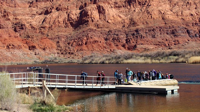 People in a line on a short boat dock board a large rubber raft.