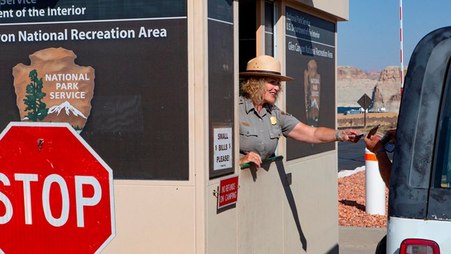 Park Ranger in fee booth reaches out to driver of car.