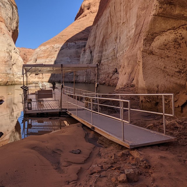 A metal and plastic dock leads back into a narrow canyon and forward on a sandy beach.
