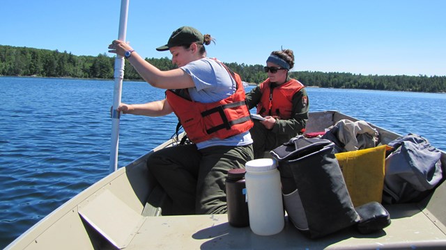 A woman in a canoe pushes a white tube down into a lake