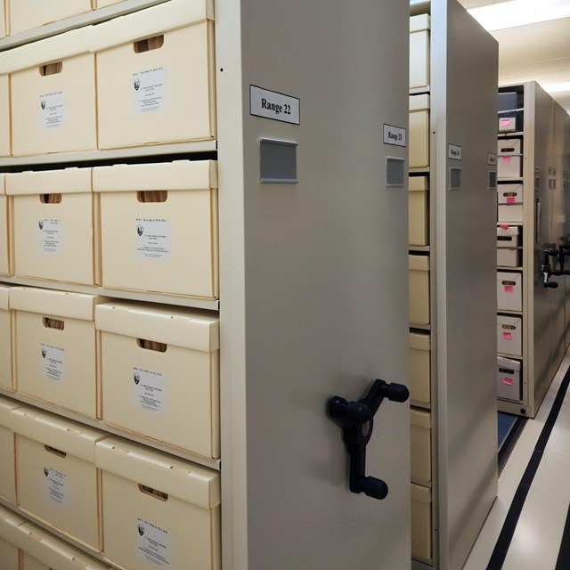 Large metal shelves filled with boxes. These shelves are on a track and moved by a crank.