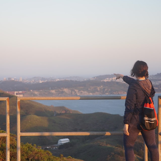 A person pointing behind a railing at the Golden Gate Bridge and San Francisco