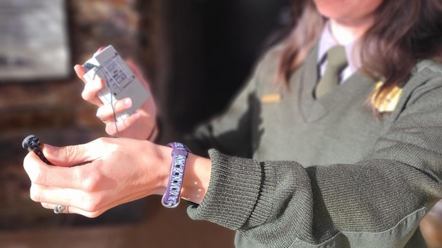 A park ranger with outstretched arms holds a small grey box in one hand and small earbud in other.