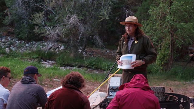 A ranger stands holding a picture at the front of a group of seated people