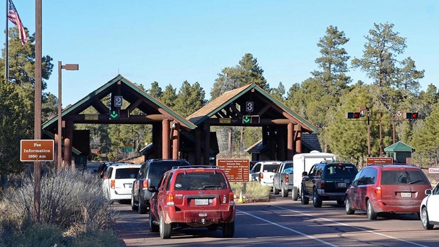 two lines of cars are waiting to buy entrance passes outside of a rustic entrance station.