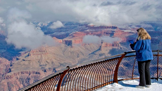 Six people taking photos at a scenic overlook as sunset illuminates a single peak in the canyon.