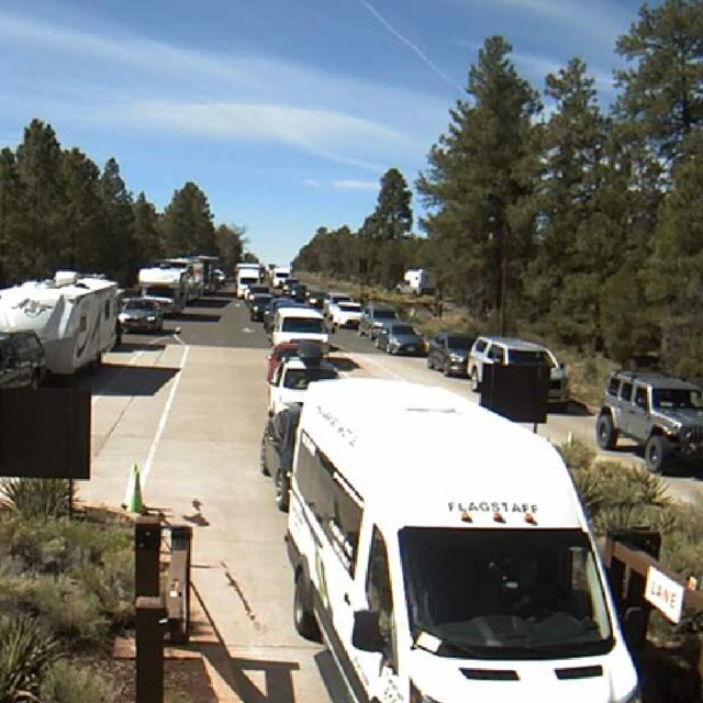 cars at an entrance station with trees surrounding the road.