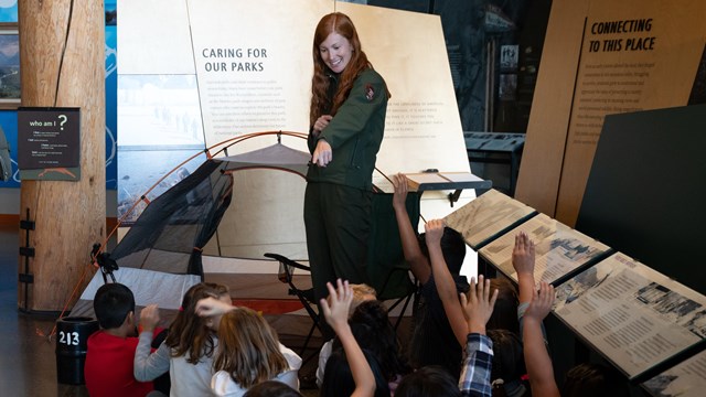 A group of students learn from a park ranger giving a talk.