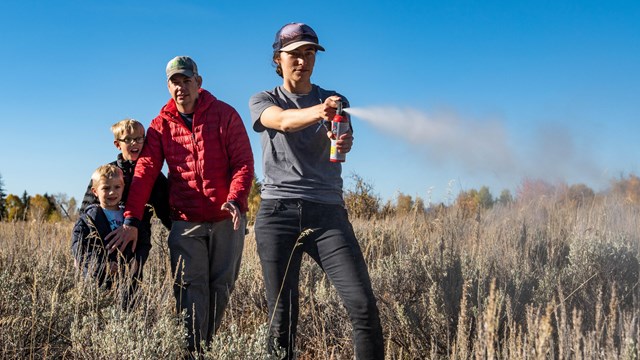 a woman sprays bear spray while a man with two kids stands behind