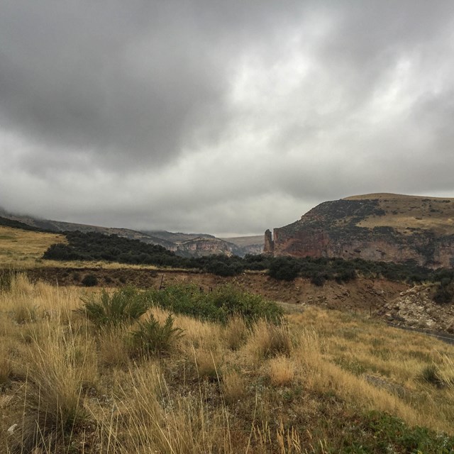 Grassy fields and distant desert hills with heavy cloud cover.