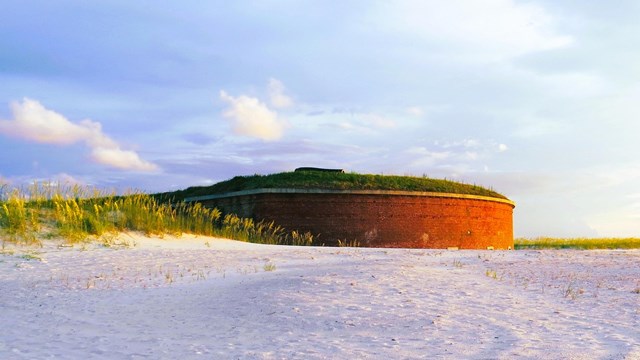 Sea oats stand in the foreground with a large masonry fort in the background.