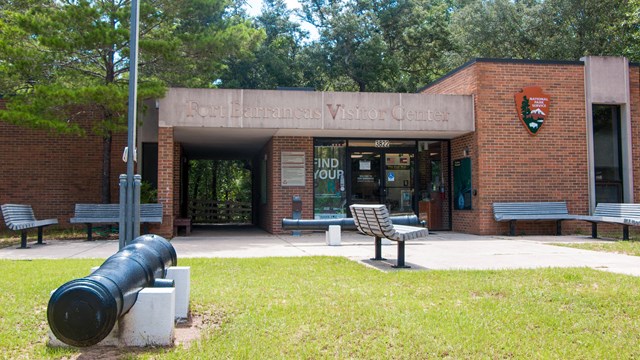 A cannon stands in front of the brick Fort Barrancas Visitor Center.