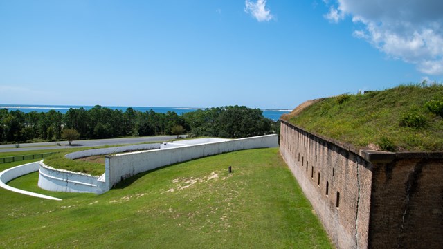 A canon peers over a brick wall with the coastline in the distance.