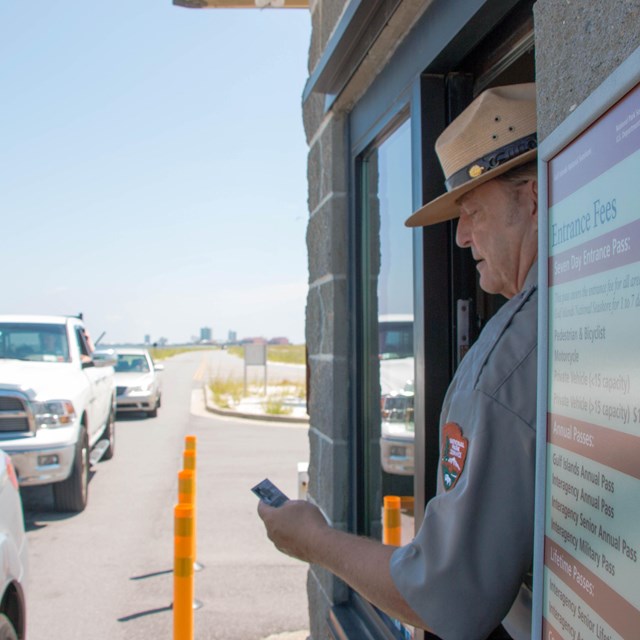 A ranger examines a park pass from an entrance gate window.