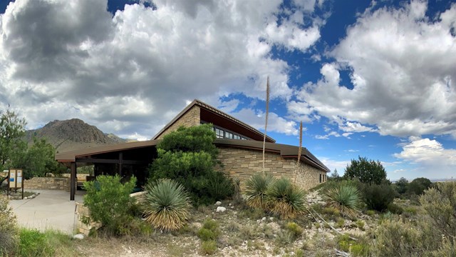 The stone walls of the visitor center stand before a desert mountain landscape