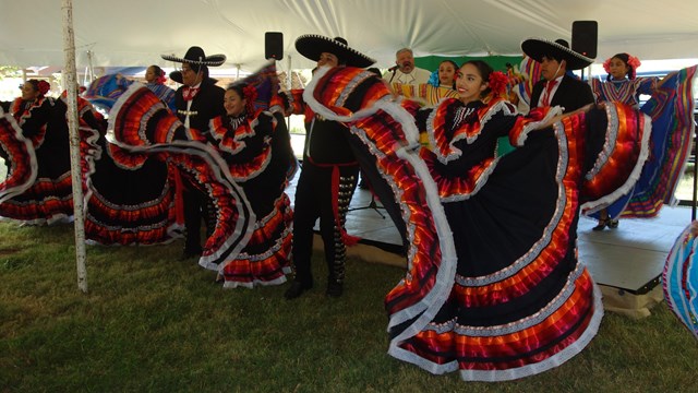 Seven dancers dressed in colorful dresses and five musicians. 