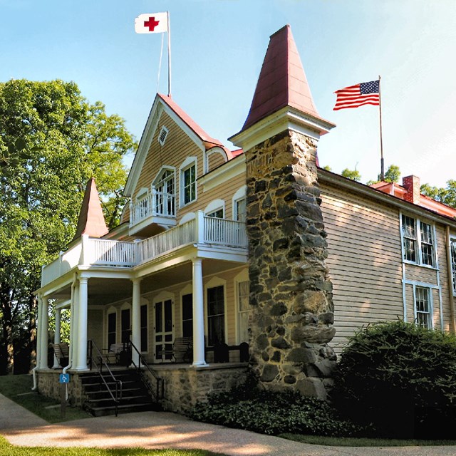 A stone and wooden home with a red cross flag flying.