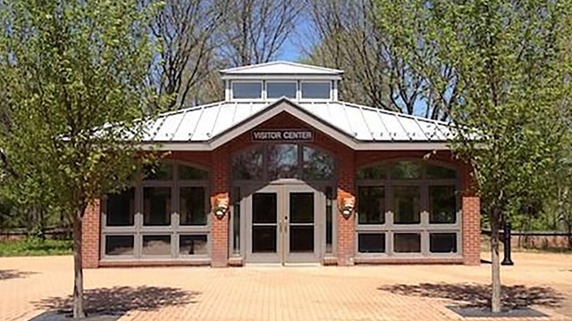 Rectangular brick building with glass double doors framed by matching sets of windows