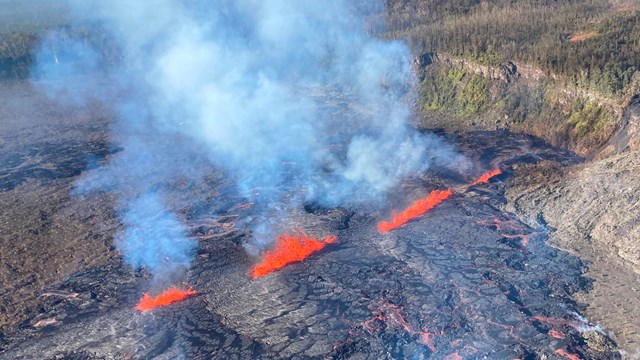 Line of bright red lava fissures inside a volcanic crater surrounded by green vegitation.