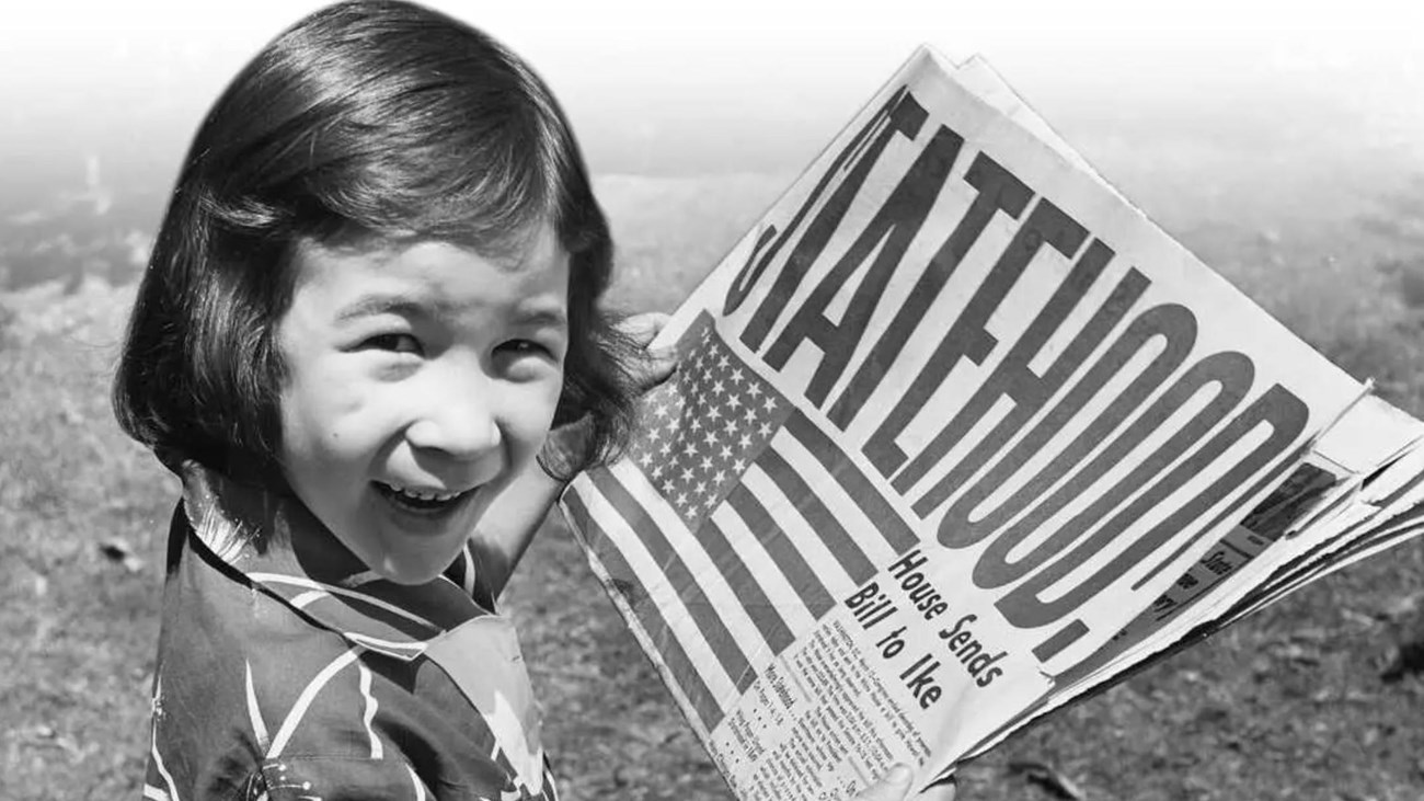 A photograph from 1959 of a young girl holding a newspaper that says statehood. 