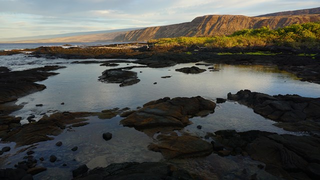 Sunrise over a small rocky bay with sun-lit cliffs beyond