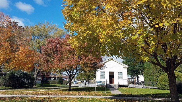 Trees in brilliant autumn foliage frame an old white schoolhouse.