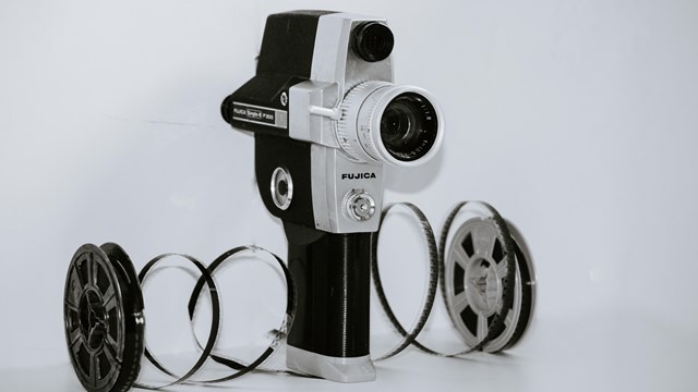 Old black and white film video camera is shown with unspooled film against a white background.