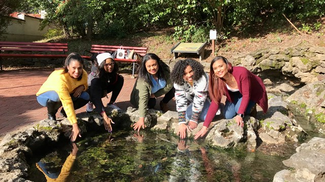 A group of young women pose with their hands in a display spring at Arlington Lawn.