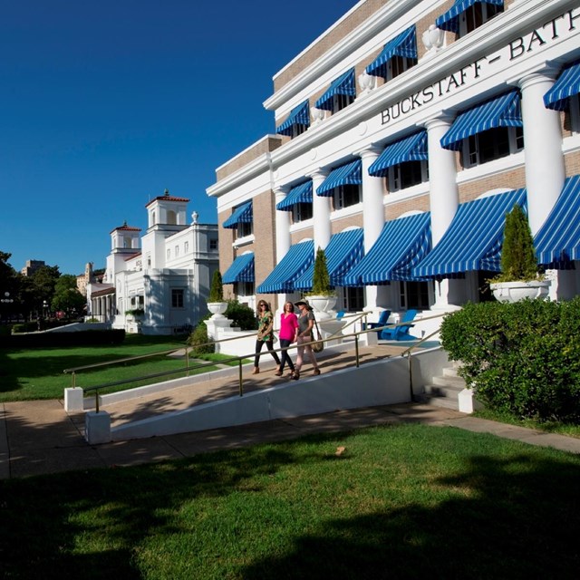 A couple walks out of a large building with blue awnings.