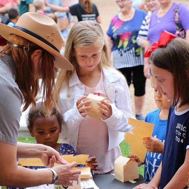 Park ranger demonstrating a craft activity to kids gathered around a table