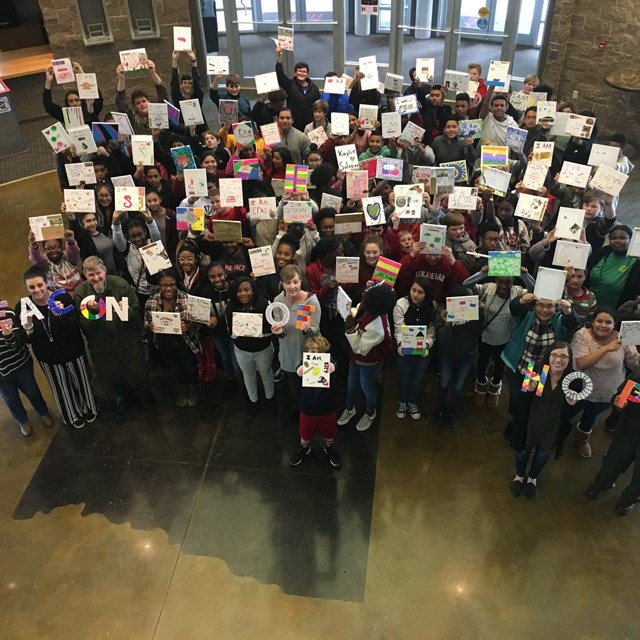 Large group of people holding up letters and signs to the camera above