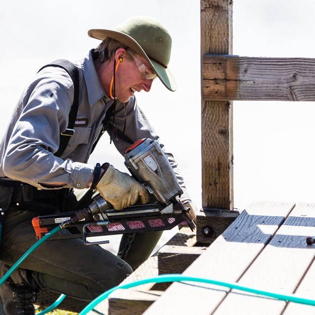 Maintenance worker using a power drill on a boardwalk