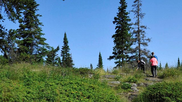 People hike up a rocky trail to a ridge top. 